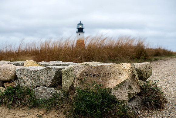 Photograph of Sankaty Head Lighthouse Nantucket with rocks, grass, and clouds in the sky