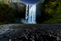 Skogafoss waterfall in souther iceland with the night sky above and rocks in the foreground