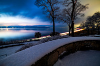 Hudson River after sunset and blue hour following a snow storm with mountains in the background and light trails from the commuter train in the foreground
