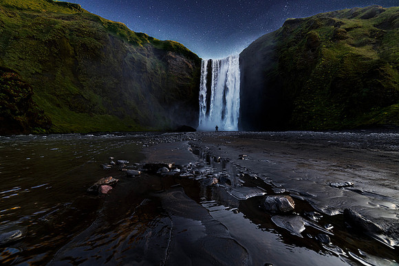 Skogafoss waterfall in souther iceland with the night sky above and rocks in the foreground